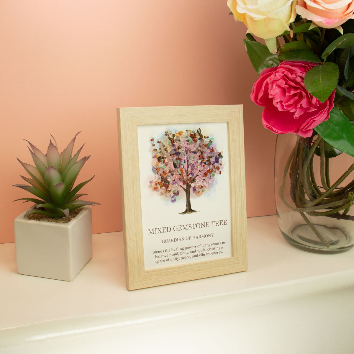 Stilvoll dekoriertes Edelsteinbild mit buntem Lebensbaum auf einem weißen Regal neben einer Pflanze und Rosen.